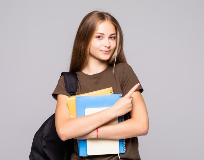 SCHOLAR - Uma adolescente segurando três apostilas entre os braços cruzados sobre a barriga